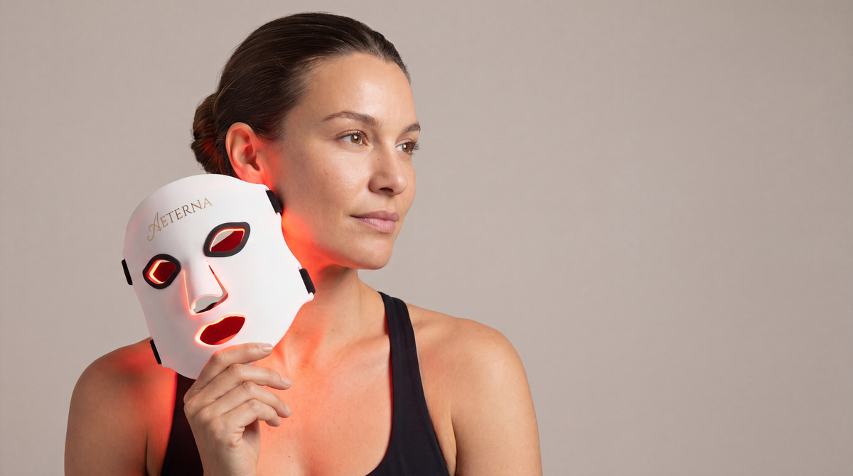 Woman holding a white LED face mask with visible branding against a plain background